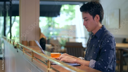 Attractive hispanic man sitting in coffee shop typing on laptop and drinking coffee, medium shot