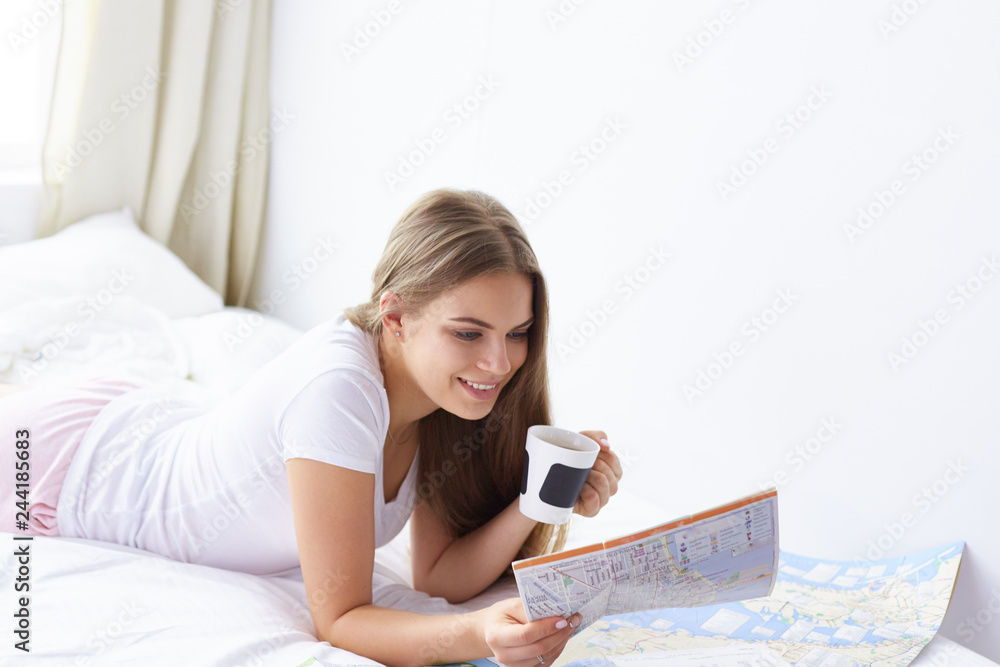 Happy young girl in bed using phone, tablet and maps to search for travel Happy young girl in bed using phone, tablet and maps to search for travel