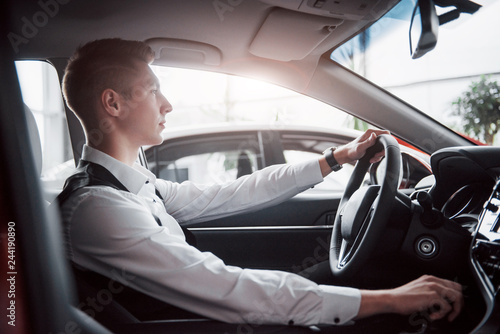 A young man sits in a newly purchased car at the wheel, a successful purchase. © standret
