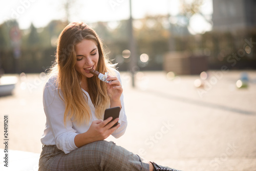 Fototapeta Teenage woman outside chatting on phone, having energy bar.