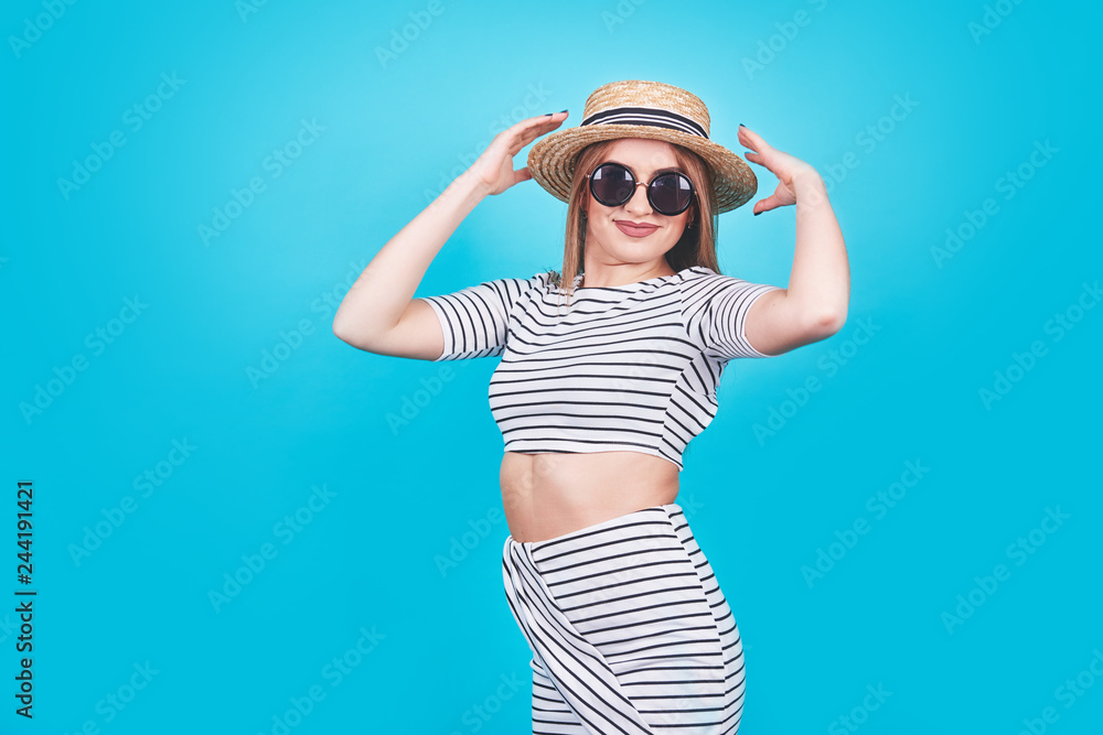 Attractive girl in a white and black stripes, hat, sunglasses, emotionally opened mouth on a bright blue background with a perfect body. Isolated. Studio shot Attractive girl in a white and black stripes, hat, sunglasses, emotionally opened mouth on a bright blue background with a perfect body. Isolated. Studio shot