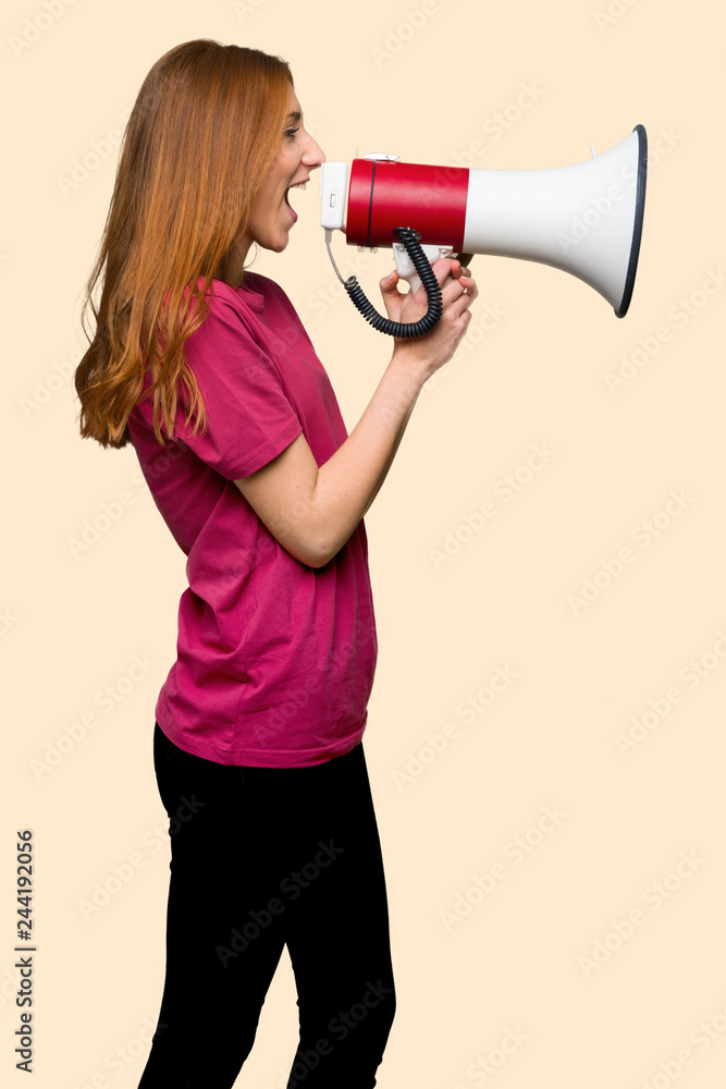 Young redhead girl shouting through a megaphone to announce something in lateral position on isolated yellow background Young redhead girl shouting through a megaphone to announce something in lateral position on isolated yellow background