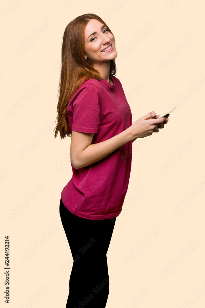 Young redhead girl sending a message with the mobile on isolated yellow background Young redhead girl sending a message with the mobile on isolated yellow background