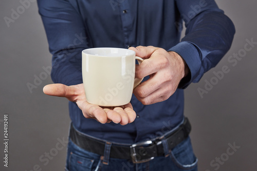 Handsome bearded man with stylish hair beard and mustache on serious face in shirt holding white cup or mug drinking tea or coffee in studio on grey background