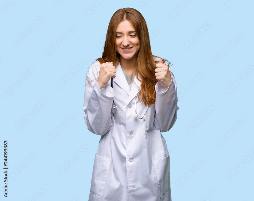 Redhead doctor woman celebrating a victory in winner position on isolated blue background Redhead doctor woman celebrating a victory in winner position on isolated blue background