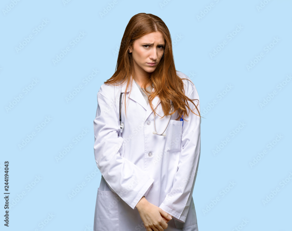 Redhead doctor woman with sad and depressed expression on isolated blue background Redhead doctor woman with sad and depressed expression on isolated blue background