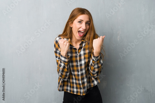 Young redhead girl over grunge wall celebrating a victory in winner position