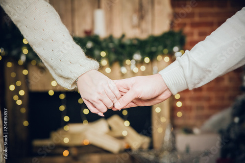 A man and a woman hold hands close-up on the background of blurry lights. Female hand on top
