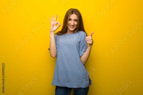 Young redhead girl over yellow wall background showing ok sign with and giving a thumb up gesture