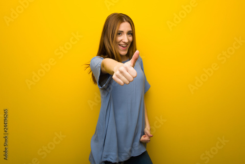 Young redhead girl over yellow wall background giving a thumbs up gesture because something good has happened © luismolinero