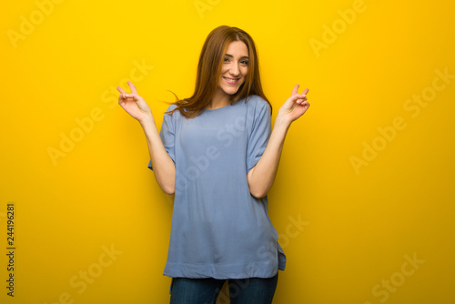 Young redhead girl over yellow wall background smiling and showing victory sign with both hands