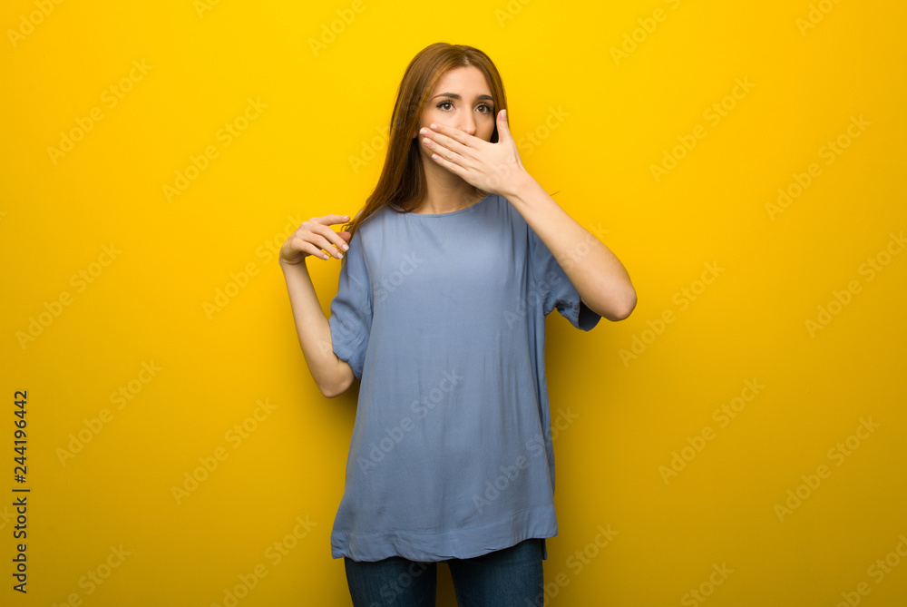 Young redhead girl over yellow wall background covering mouth with hands for saying something inappropriate Young redhead girl over yellow wall background covering mouth with hands for saying something inappropriate