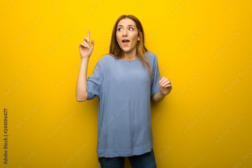 Young redhead girl over yellow wall background intending to realizes the solution while lifting a finger up