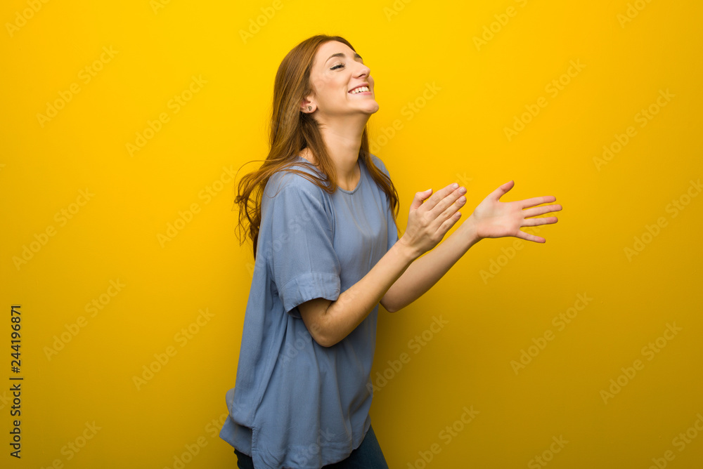 Young redhead girl over yellow wall background applauding after presentation in a conference Young redhead girl over yellow wall background applauding after presentation in a conference