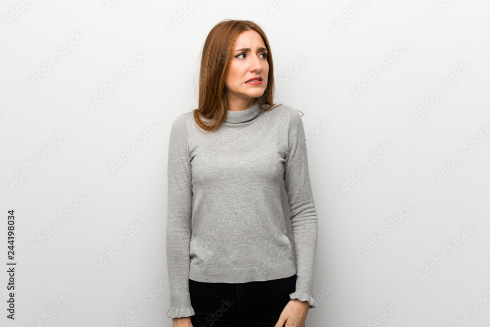 Redhead girl over white wall is a little bit nervous and scared pressing the teeth Redhead girl over white wall is a little bit nervous and scared pressing the teeth