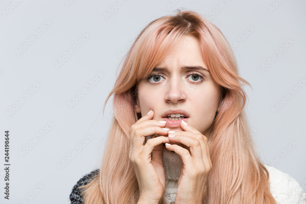 Close up studio portrait of nervous student in white sweater, gnawing nails, looking in camera/girl in a stupor, found out what happened, bad news, nervous feeling, experiences of fear/people concept Close up studio portrait of nervous student in white sweater, gnawing nails, looking in camera/girl in a stupor, found out what happened, bad news, nervous feeling, experiences of fear/people concept