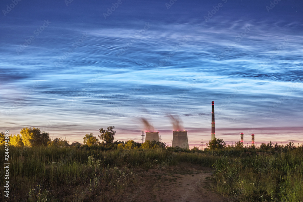 Noctilucent clouds in the summer night sky against the background of a thermal power station