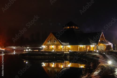 Wooden restaurant near the frozen pond in sunset, winter cloudy day