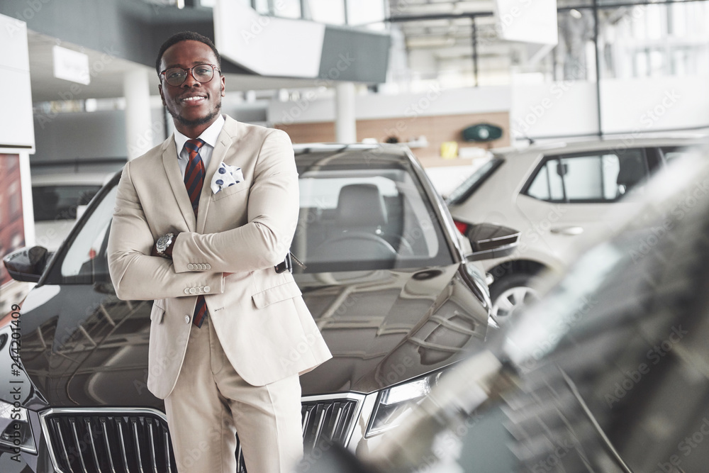 Young black businessman on auto salon background. Car sale and rent concept Young black businessman on auto salon background. Car sale and rent concept