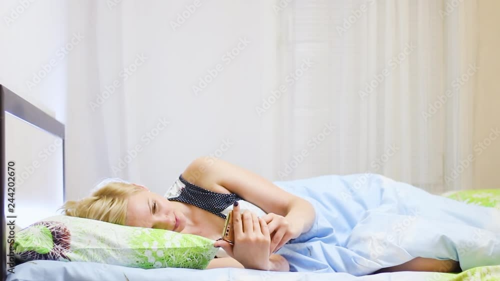 beautiful young blonde girl lies on bed and uses smartphone beautiful young blonde girl lies on bed and uses smartphone