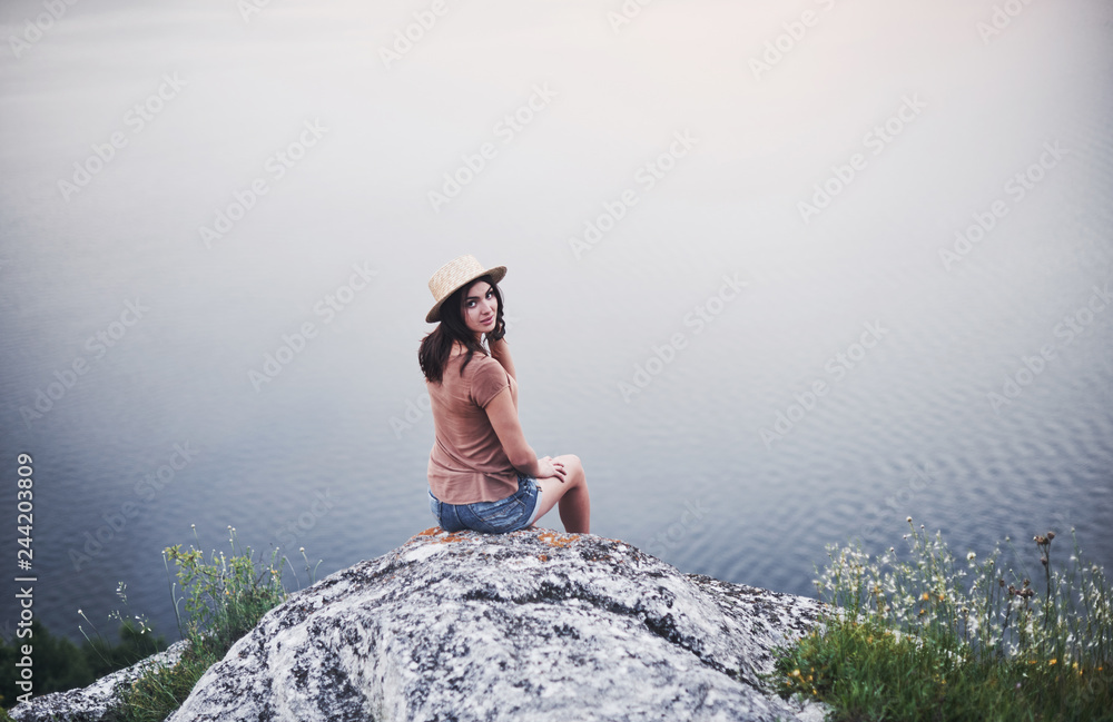 View from the back. Attractive tourist girl posing at the edge of mountain with clear water lake in background View from the back. Attractive tourist girl posing at the edge of mountain with clear water lake in background