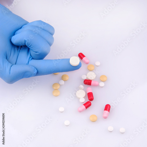 a hand of a doctor in blue glove holding a white pill near other capsules