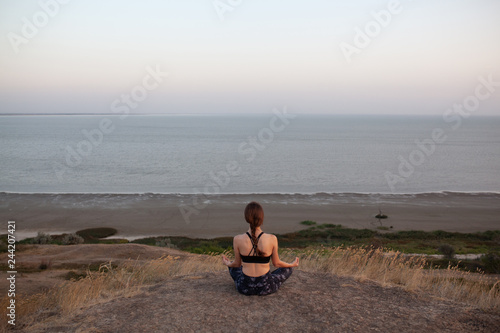 Anonymous young girl Practicing Yoga in Lotus pose sitting on the edge of rock against of see. Padmasana