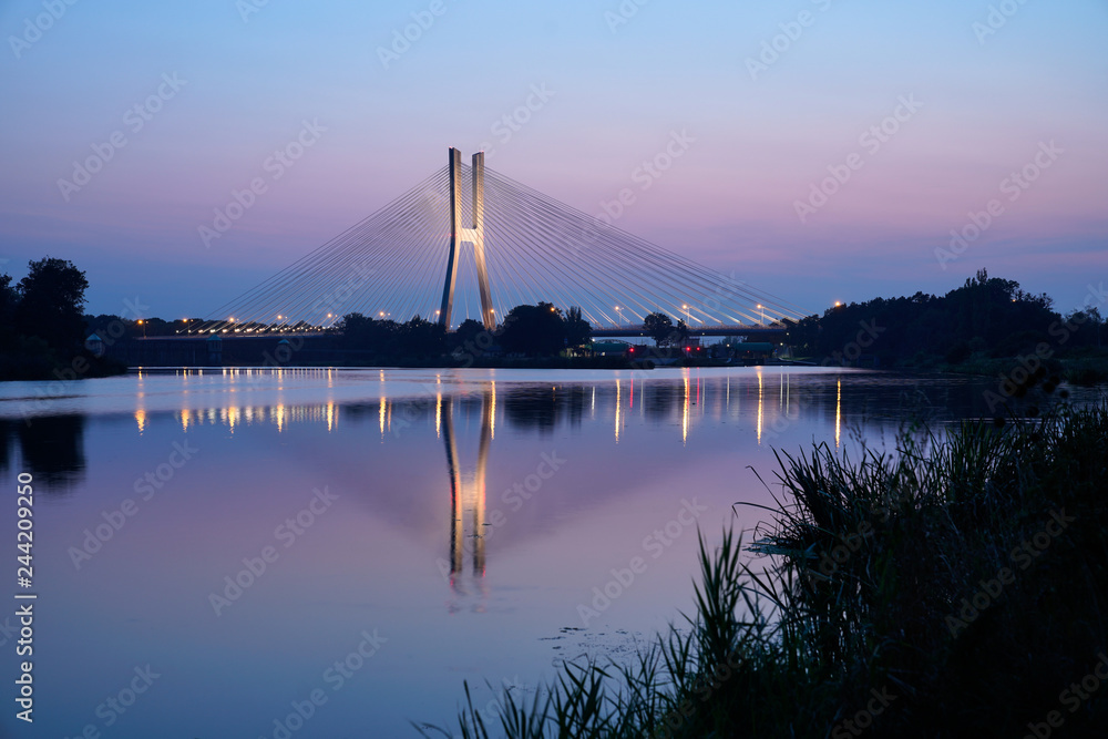 Fototapeta premium Modern illuminated bridge reflecting in water on a warm summer evening