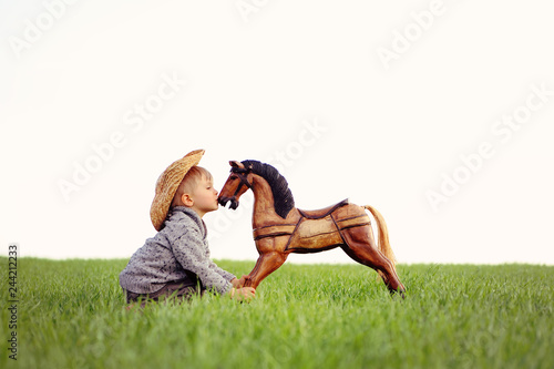 A boy, three years old, playing his toy rocking horse, dreaming about a real horse. a concept of true friendship and selfless love. Happy childhood in the countryside, the child takes care his pet.