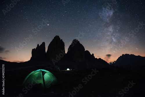 Our galaxy is on the sky. Two lighting tents with tourists inside near the Tre Cime three peaks mountains at night time