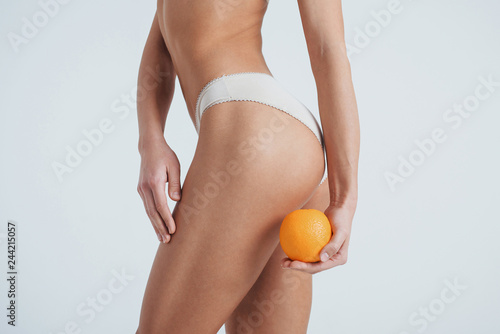 Fitness conception. Photo of girl in underwear turning left side of the body to the camera and holding orange in her hand