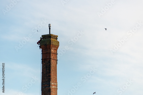 Foto man doing a dangerous steeplejack job climbs of top of high chimney to make repa