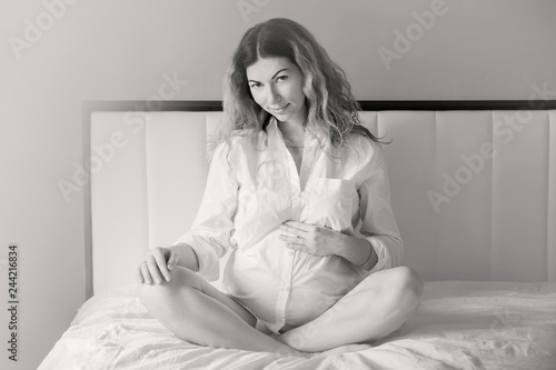 Attractive pregnant woman is sitting in bed and holding her belly