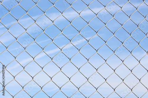 A close up photograph of a section of wire fencing, against a blue sky. Security, safety concept. Barrier