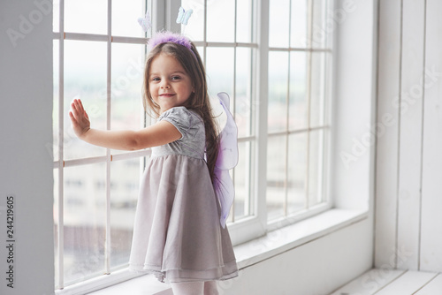 Touching the glass. Nice little girl in the fairy tale wear standing near the windows and looking into the camera Free Download Touching the glass. Nice little girl in the fairy tale wear standing near the windows and looking into the camera - GFXLoad