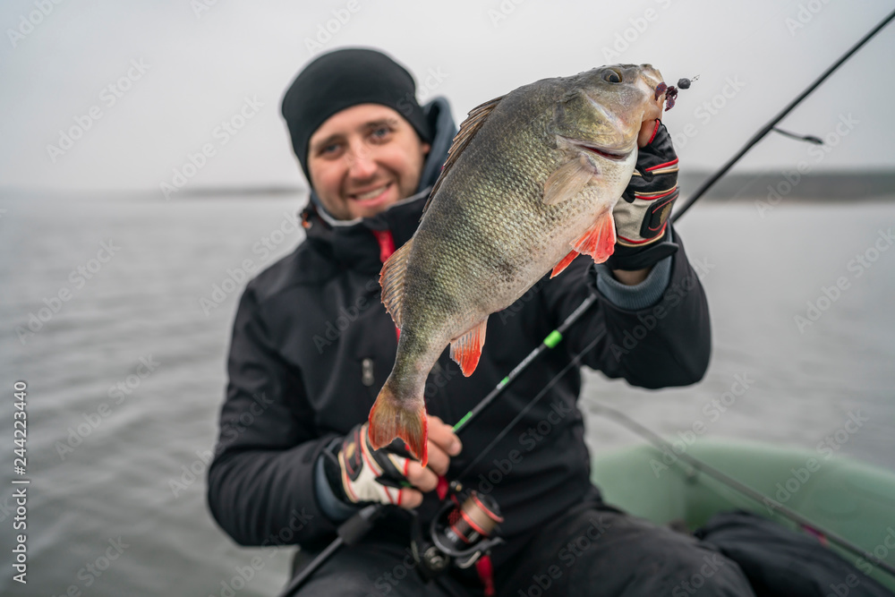 Happy fisherman with big perch fish trophy at boat Happy fisherman with big perch fish trophy at boat