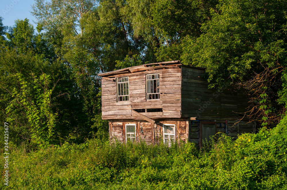 Obraz premium Light blue sky in the warm summer over the old abondoned house built from wood far away in the forest. Green trees near. Travelling on the suburb roads 