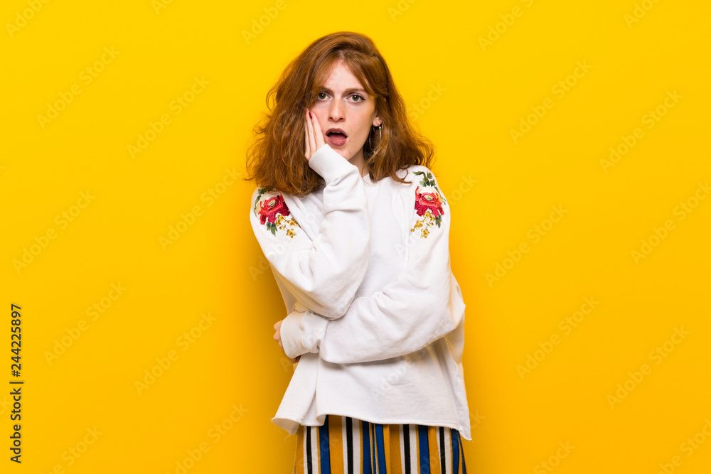 Young redhead woman over yellow wall surprised and shocked while looking right Young redhead woman over yellow wall surprised and shocked while looking right
