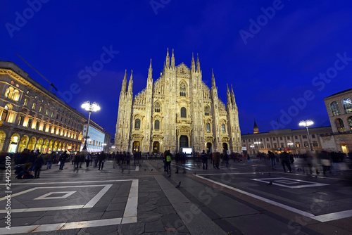 Gothic architecture of Milan Cathedral at night in Milan Italy with purposely blurred unrecognizable crowd of people in square