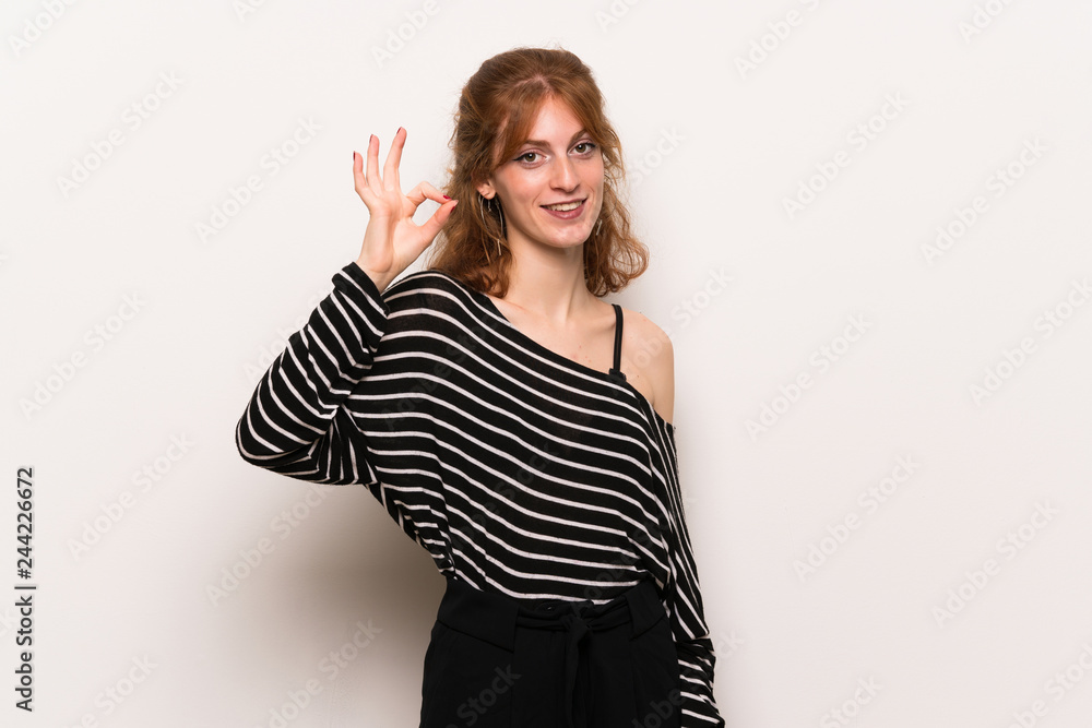 Young redhead woman over white wall showing an ok sign with fingers Young redhead woman over white wall showing an ok sign with fingers