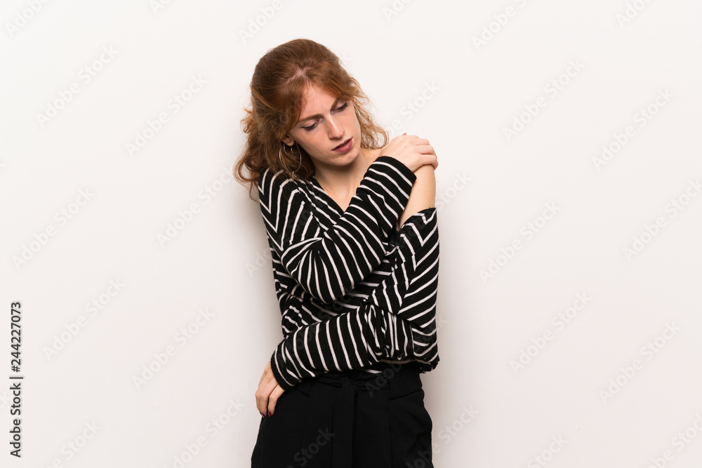 Young redhead woman over white wall suffering from pain in shoulder for having made an effort Young redhead woman over white wall suffering from pain in shoulder for having made an effort