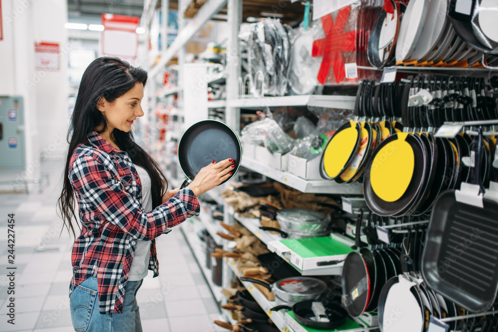 Young woman choosing frying pan in supermarket