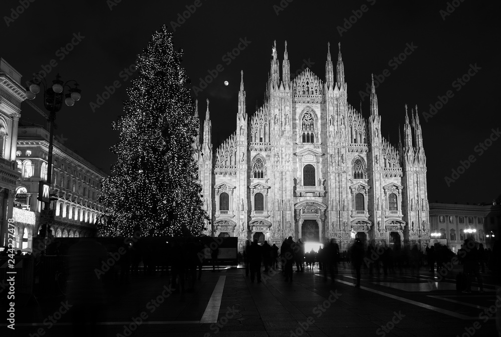 Gothic architecture of Milan Cathedral at night with moon in Milan Italy with purposely blurred unrecognizable crowd of people in square