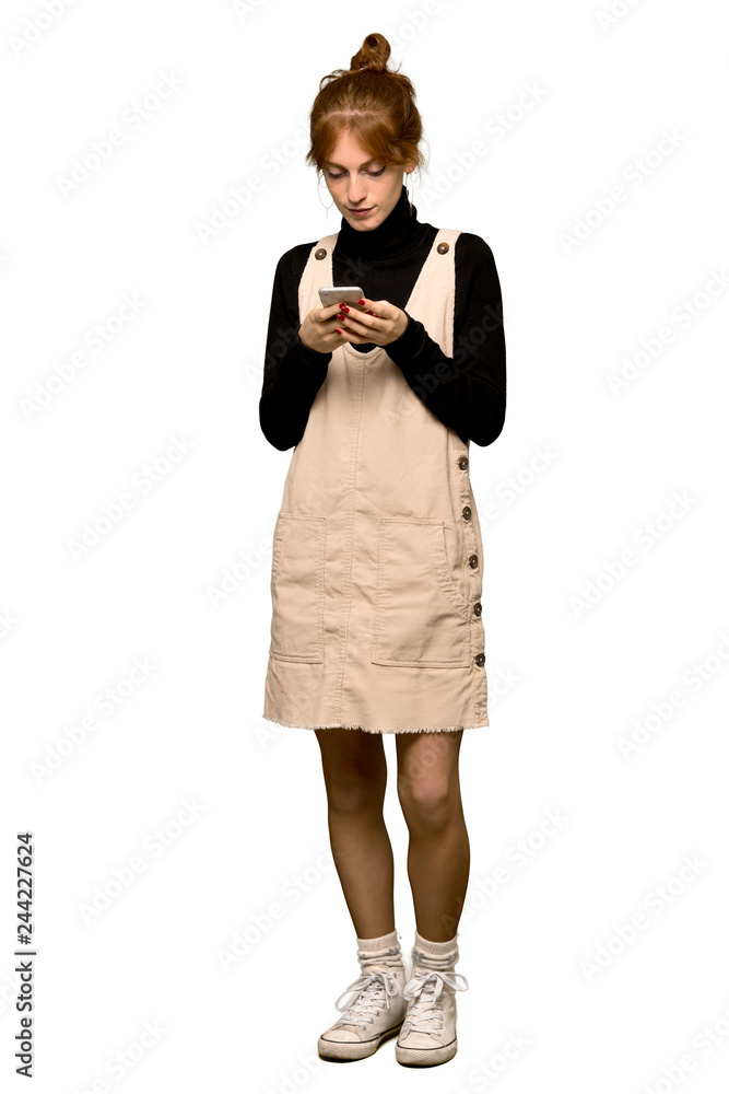 A full-length shot of a Young redhead woman sending a message with the mobile over isolated white background A full-length shot of a Young redhead woman sending a message with the mobile over isolated white background