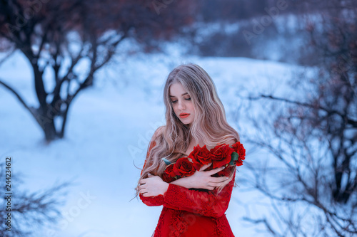 magical image of attractive blonde girl in gorgeous red dress decorated with flowers, Rose princess trying to keep warm in snowy forest, wonderful work of make-up by visagiste and photographer photo