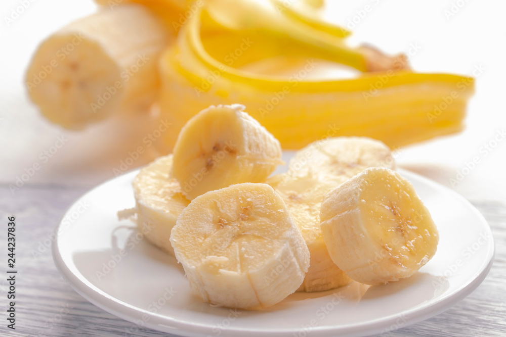 Sliced banana on a white plate and a light wooden table. Pink burning candle nearby.