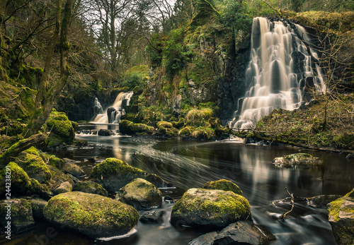 Long exposure shot of Linn Jaw Waterfalls, near Livingston, Scotland, with mossy rocks in the foreground and surrounding the waterfalls and white foam streaks in the water. West Lothian. UK. Nature. L photo