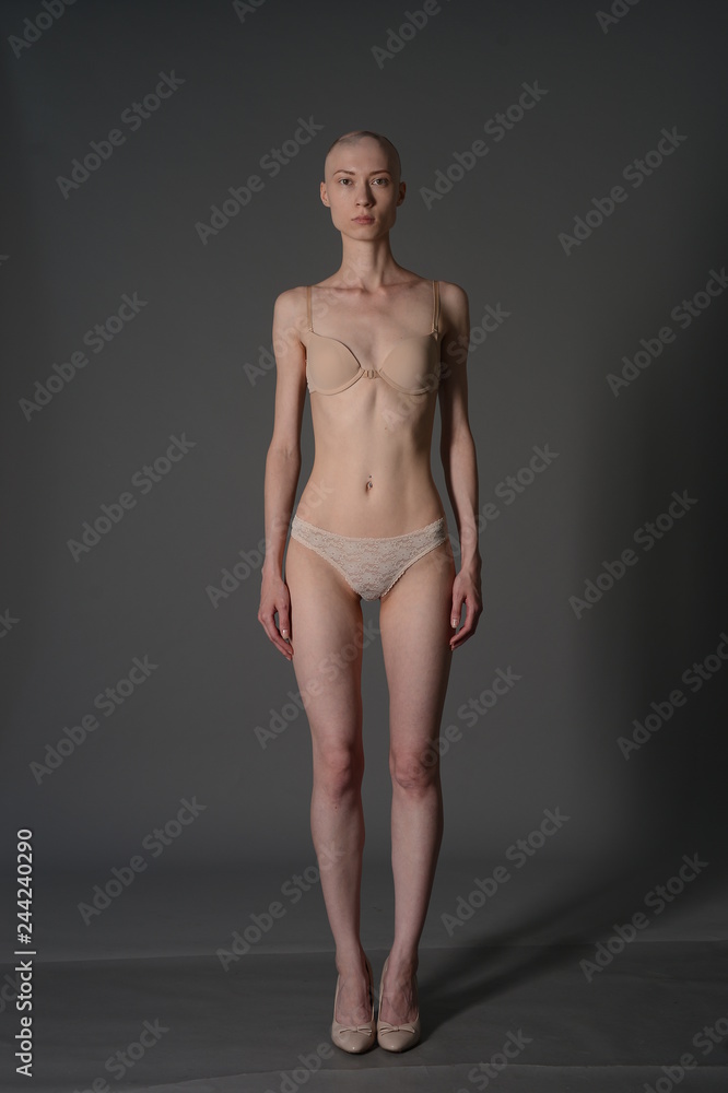 Naklejka premium bald girl in beige lingerie posing on grey background