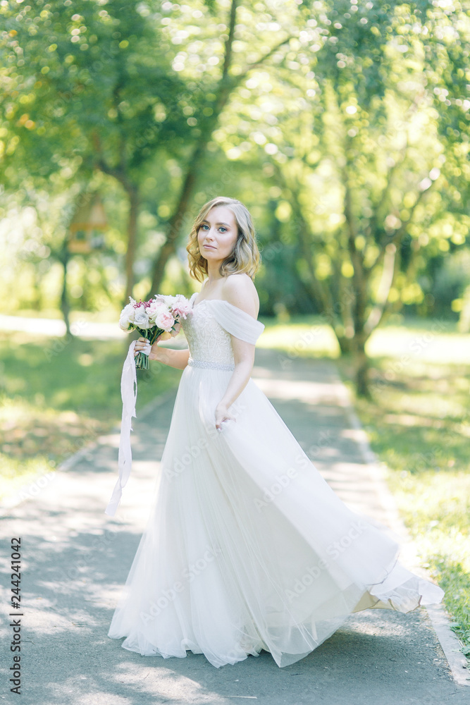 The bride in a white dress in nature in the Park. Photo shoot with a bouquet in the style of fine art.