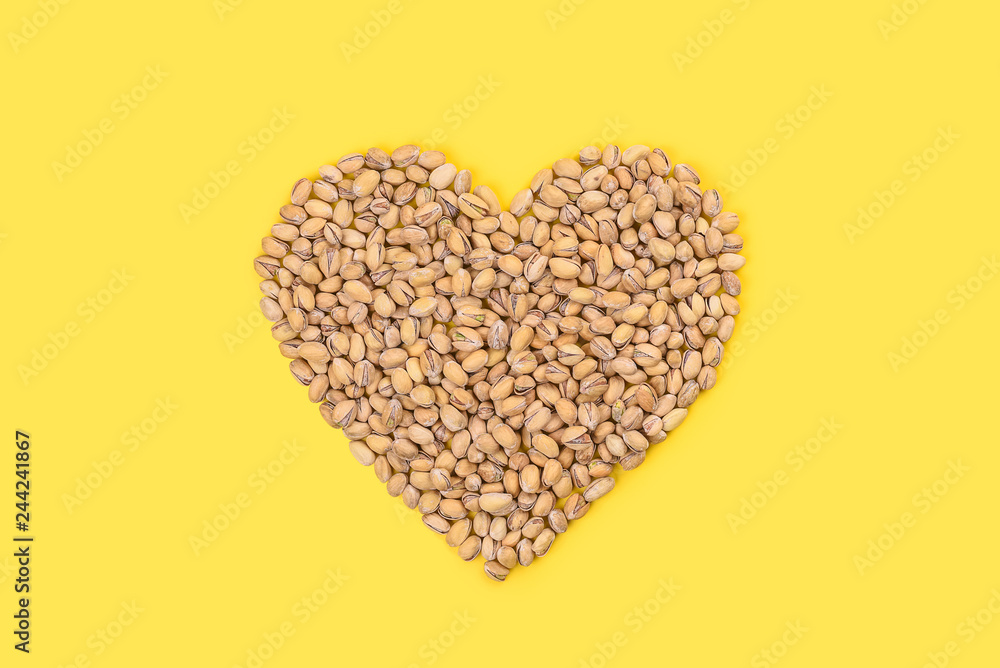 Heart of pistachios on a bright yellow background.